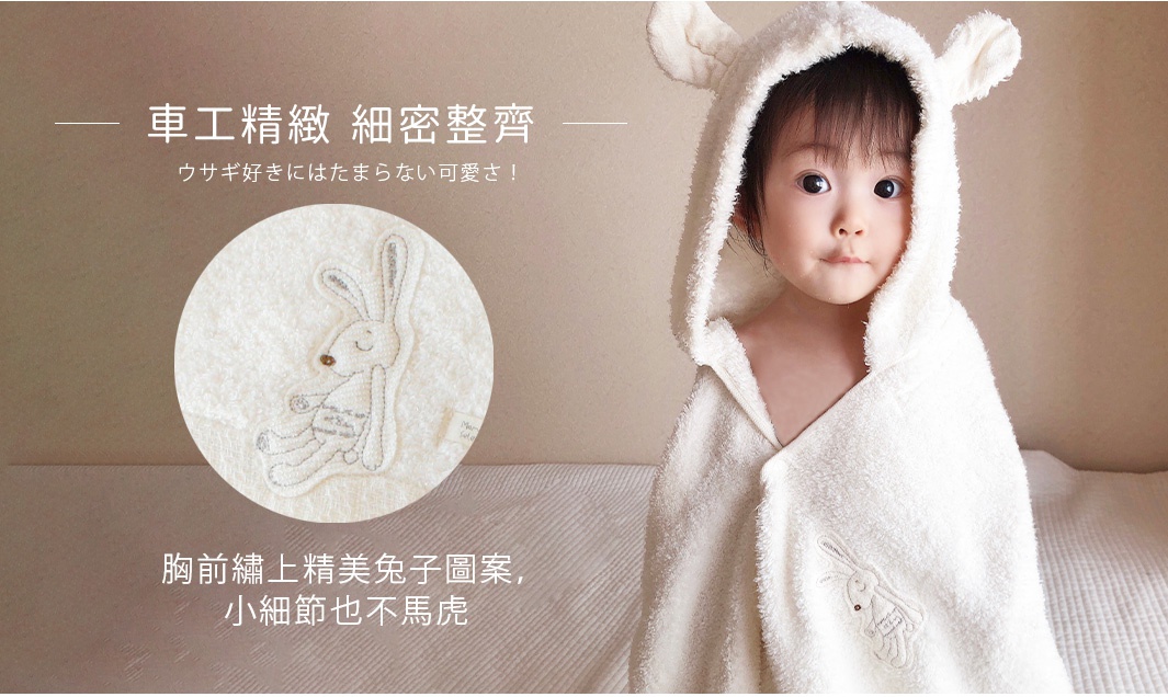 一位可愛的嬰兒穿著一件厚實的米白色連帽浴巾，浴巾上有精緻的兔耳朵設計，胸前繡有可愛的兔子圖案。
