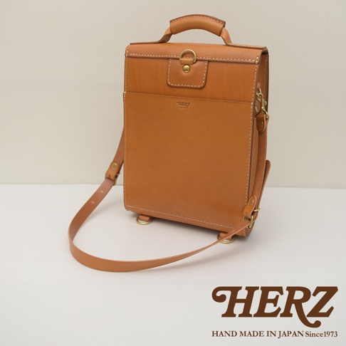 職人手作皮革復古後背包，採用天然棕色皮革，設計簡潔，有頂部提把、翻蓋開合及正面貼袋，配有可調節式肩帶。