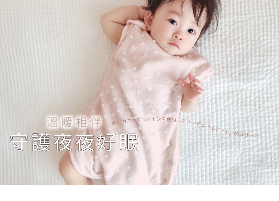 粉色紗布材質的嬰兒連身衣，表面帶有白色小圓點圖案，由一位嬰兒穿著，躺在白色紋理的床鋪上。