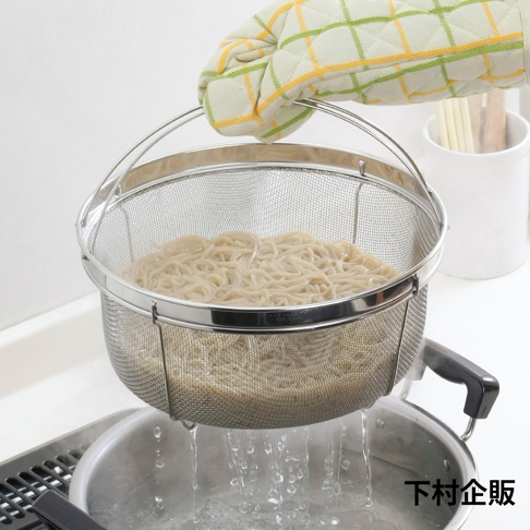 一只戴著隔熱手套的手正提起一個裝滿麵條的不鏽鋼網籃，網籃內有細緻的網眼，邊緣有金屬環，底部有三個支撐腳，正在瀝乾水分。