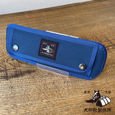 深藍色純棉帆布筆袋，設有金屬按扣及品牌標籤，標籤印有黑犬及日文字樣。