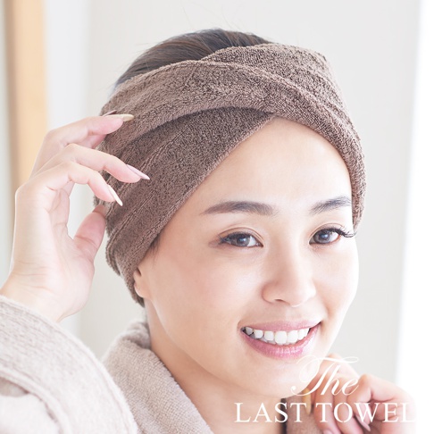 一位女子戴著棕色毛巾髮帶，臉部特寫，她穿著一件淺棕色浴袍，手輕輕觸碰髮帶。