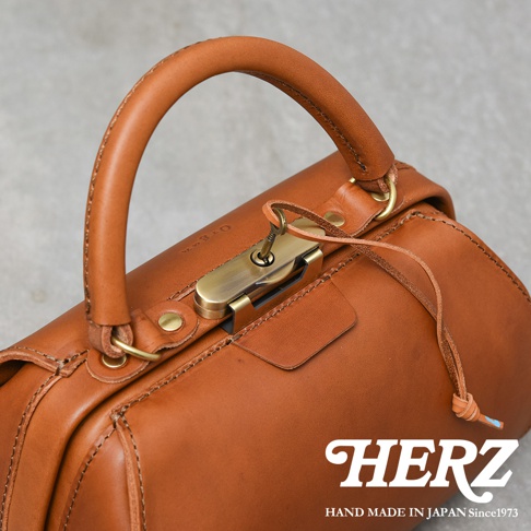 職人手作皮革Organ兩用口金手提包，整體為棕褐色，包身由光滑的皮革製成，配有黃銅色金屬口金鎖和鑰匙。