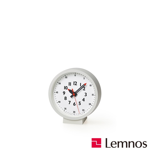淺灰色圓形桌面時鐘，白色錶盤，黑色時針、分針，紅色秒針。錶盤外圍標有分鐘刻度，內圈為小時數字，設計簡潔。