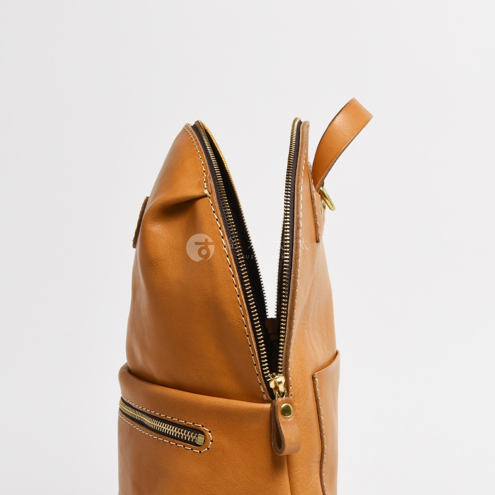 棕色皮革製成的大開口圓角後背包，拉鍊半開，露出內部，金色拉鍊五金配件，簡潔的設計，展現皮革紋理。