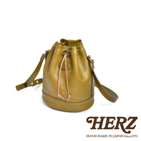 職人手作皮革束口單肩包，呈現橄欖綠色，採用光滑皮革材質，束口設計搭配粉紅色抽繩，附有可調節的單肩背帶。