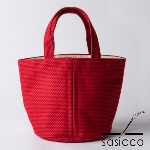 紅色三河木綿刺子織圓底水桶包，具有標誌性的織紋和圓潤包身，搭配簡單的提把，展現日式簡約風格。