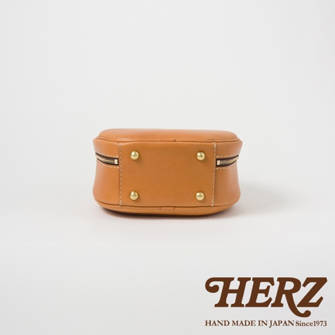 HERZ 職人手作皮革兩用圓形包 Q-13，駝色，底部有四顆金屬腳釘，側邊有拉鍊。
