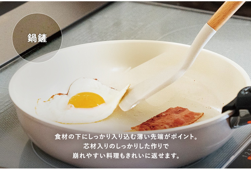 一個淺奶油色平底鍋，鍋中煎著一個太陽蛋和一片培根，一個白色的鍋鏟，帶有木製手柄，正在翻動食物。左上角圓形標示寫著「鍋鏟」。