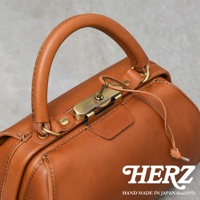 職人手作皮革Organ兩用口金手提包，整體為棕褐色，包身由光滑的皮革製成，配有黃銅色金屬口金鎖和鑰匙。