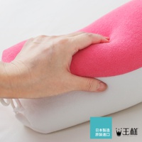 一隻手按壓著粉紅色的圓柱形糖果枕，枕頭上半部是粉紅色絨毛材質，下半部是白色絨毛材質，枕頭兩側有白色繫繩。