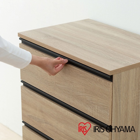 淺木紋色三層收納櫃，櫃體側面與抽屜面板皆為木紋材質，搭配黑色嵌入式抽屜把手，由左側伸出的手正在開啟其中一個抽屜。