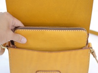 職人手作皮革寬扣帶馬鞍包，明亮的橘黃色皮革，包內可見一個拉鍊長夾，由細緻縫線固定。