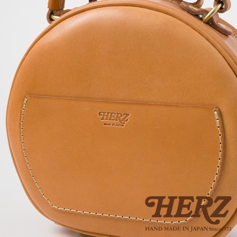 HERZ 品牌皮革圓形包，正面有壓印的品牌標誌和「MADE IN JAPAN」字樣。