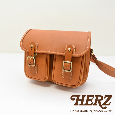 日本HERZ職人手作皮革經典雙扣郵差包，棕褐色，正面有兩個翻蓋口袋和雙扣設計，搭配可調節的肩帶。