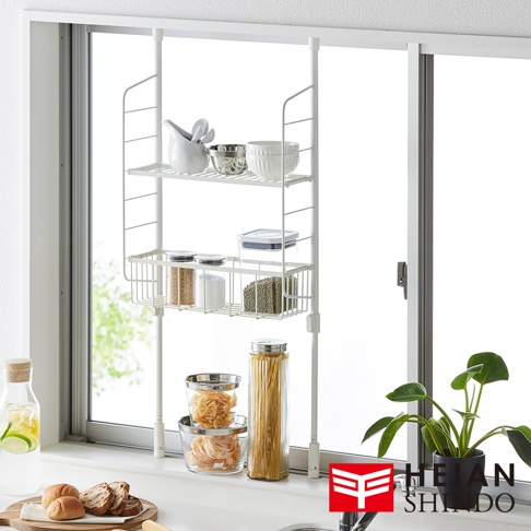 平安伸銅廚衛兩用收納籃架 SPL-4WH，架設在窗邊，收納各種廚房用品，包含碗盤、食材罐和義大利麵。