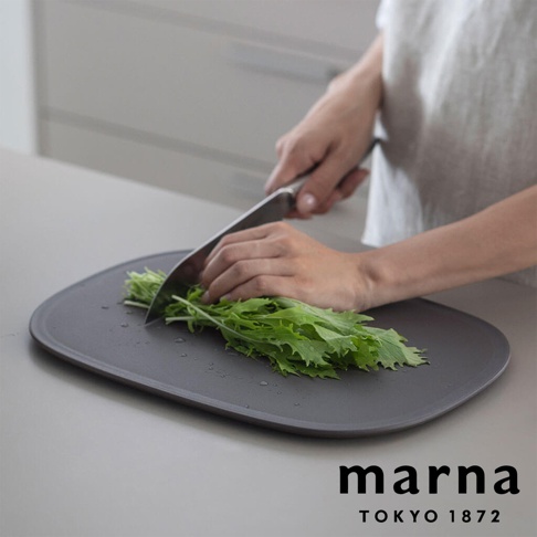 marna TOKYO 1872 品牌砧板上，一雙手正在切綠色蔬菜，砧板有少量水珠。