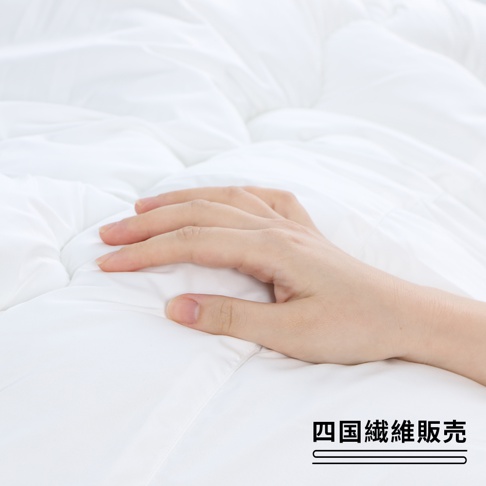 手輕柔地撫摸著純白的棉被，下方有「四國纖維販売」的日文文字標記。