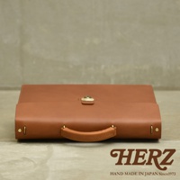 職人手作皮革Organ兩用商務公事包 G-93，採用鞣製皮革製成，呈現溫潤的棕褐色。包款設計簡潔，配有金色金屬鎖扣和手提把，側面有鉚釘裝飾。