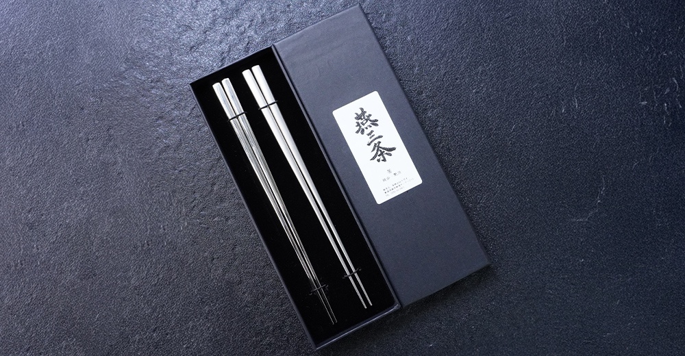 燕三条不鏽鋼筷組合，兩雙銀色拋光筷子，置於黑色包裝盒內，盒蓋上有日文標籤。