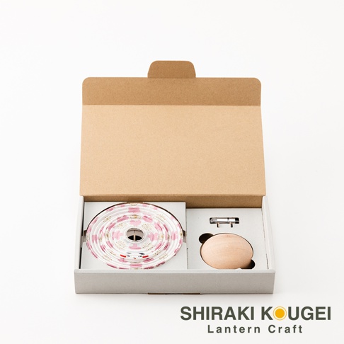 一組 cocolan 達摩不倒翁八女迷你裝飾提燈，內含白色燈帶，印有粉色和金色的日式格紋圖案，以及一個木製圓形底座和電池盒。