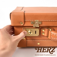 職人手作皮革英倫風便攜手提行李箱，展示皮革材質的質感與金屬鎖扣的細節，一隻手正操作著行李箱的鎖。