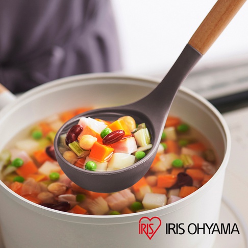 深灰色湯勺舀起一勺蔬菜湯，湯勺帶有木質手柄，湯中有紅蘿蔔、馬鈴薯、豌豆、玉米粒、豆類和肉塊。