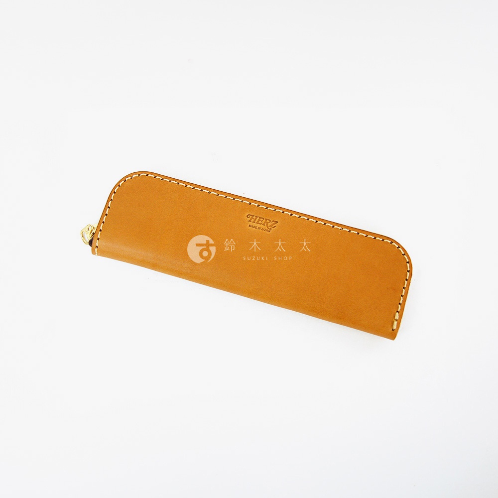 一個 tan 色皮革製成的筆袋，上面印有 HERZ MADE IN JAPAN 和 鈴木太太 SUZUKI SHOP 的字樣。