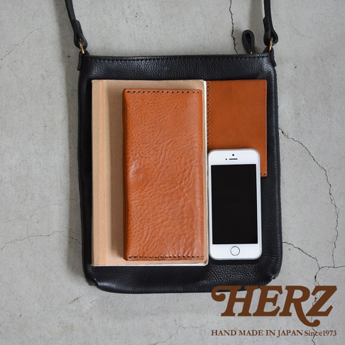 黑色皮革肩背包，內含一個棕色皮革長夾、一本淺棕色筆記本和一個白色手機。