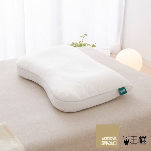 白色天絲枕套，表面有細緻紋理，枕頭呈現人體工學曲線設計，枕套一角有綠色品牌標籤。