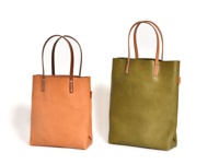 兩款職人手作皮革直式軟皮托特包，一款為淺棕色，另一款為橄欖綠色，均採用自然皮革材質，配有簡潔的提把與縫線細節。
