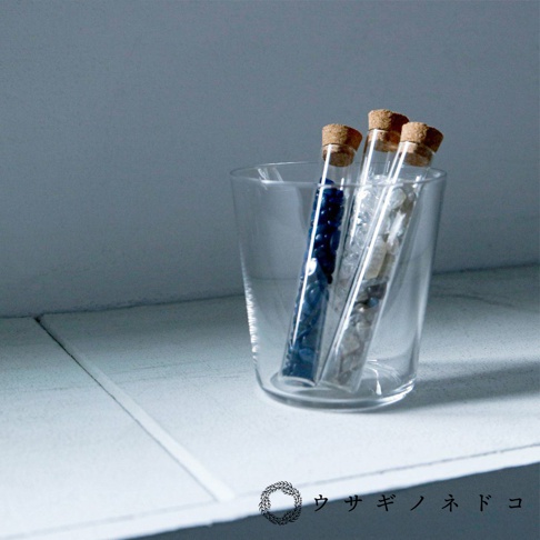 玻璃杯中裝有三個帶軟木塞的試管，試管內分別裝有藍色小顆粒、米白色和灰色碎石。