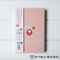 粉色美濃和紙製成的御朱印帳，封面中央印有紅色達摩吉祥物圖案，搭配一朵小紅花和藍色箭頭圖案。左側紙帶印有日文說明及多個印章圖案。