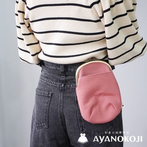 一款粉色帆布材質的腰掛口金包，附掛在身穿條紋上衣和牛仔褲的模特兒的腰部。