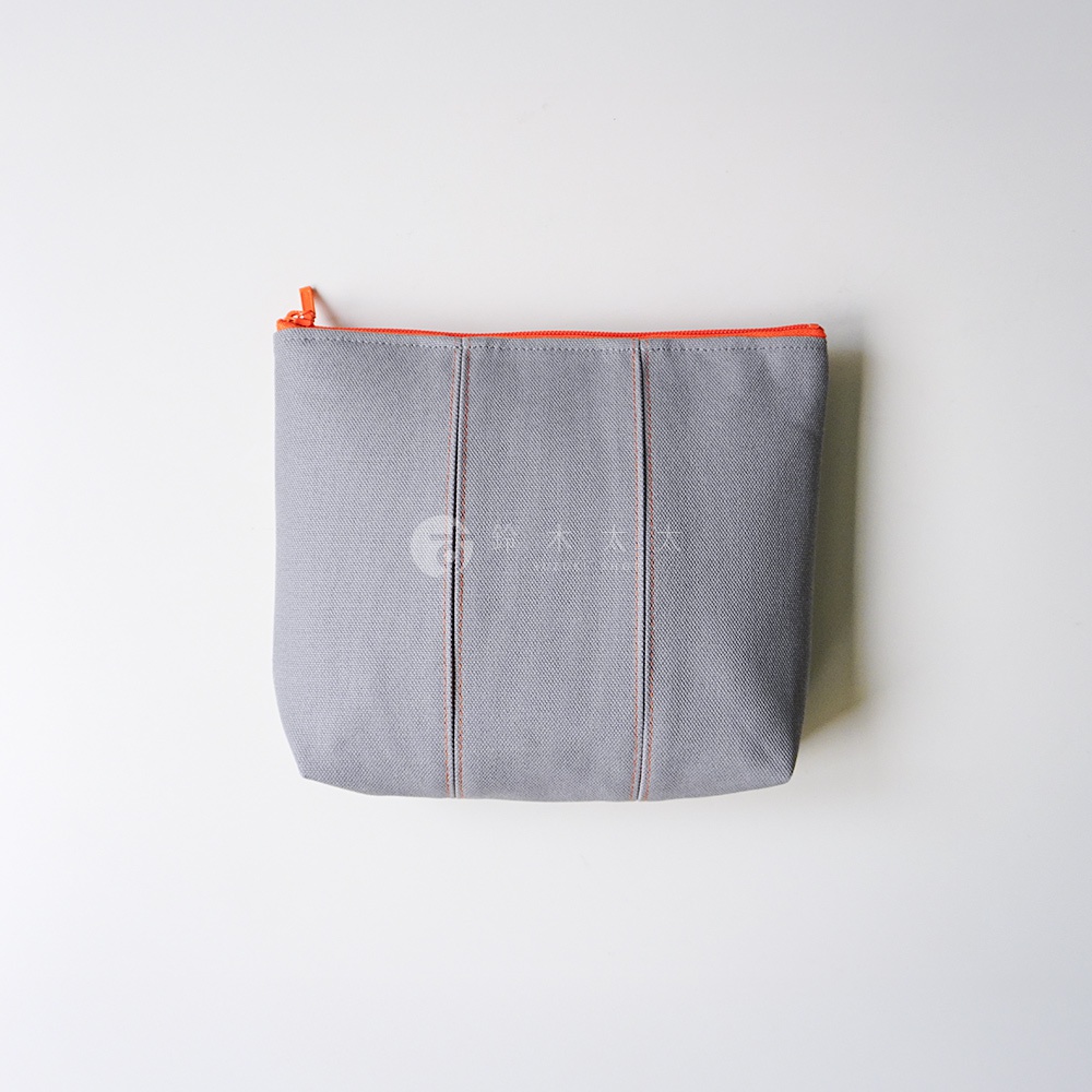 一個灰色的京都KOSHO帆布化妝收納包，正面有兩道對稱的垂直車縫線裝飾，搭配亮橘色的拉鍊，呈現簡約俐落的風格，平放在純白色背景上。