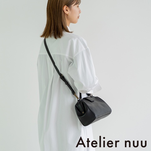 Atelier nuu 黑色皮革迷你兩用包，由側面展示，搭配白色長袖襯衫。