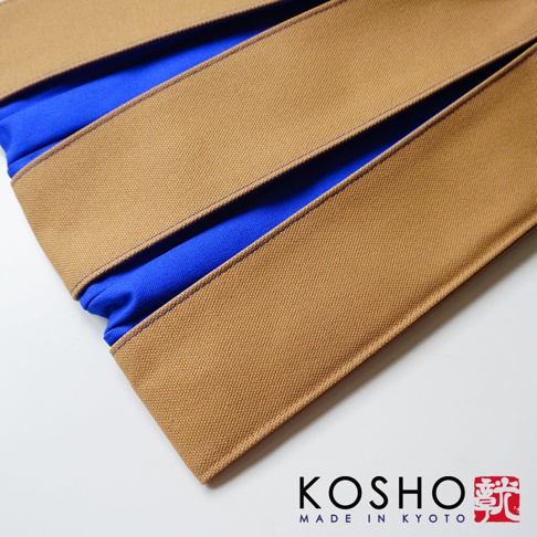 京都KOSHO品牌帆布信玄袋，外層選用質感厚實的棕色帆布，內襯為對比鮮明的亮藍色布料，呈現層次分明的摺疊設計，整體展現簡約洗練的日式工藝風格。