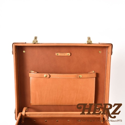 職人手作皮革英倫風便攜手提行李箱 TR-1，展示其內部結構，採用溫暖的棕色皮革材質，配有黃銅色金屬扣件和品牌標誌，內部設有實用的皮革收納袋。