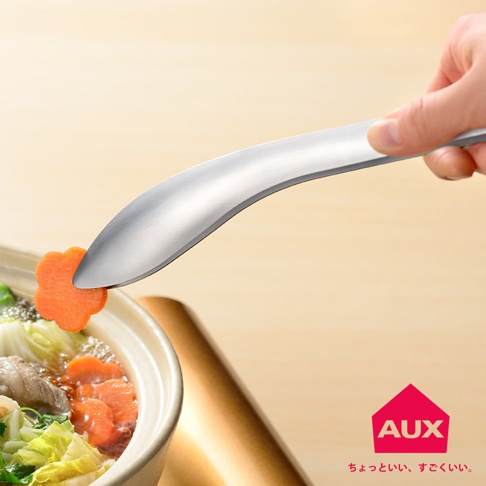 手持銀色不鏽鋼曲型分菜夾，夾取一片橘色花形紅蘿蔔，準備放入裝有蔬菜、肉類和紅蘿蔔的鍋中。