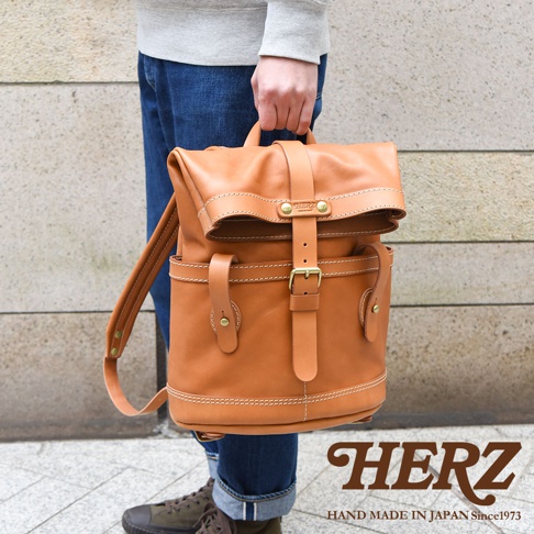 棕色皮革製雙口袋折蓋後背包，配有金屬扣環和車縫線細節，由人攜帶。