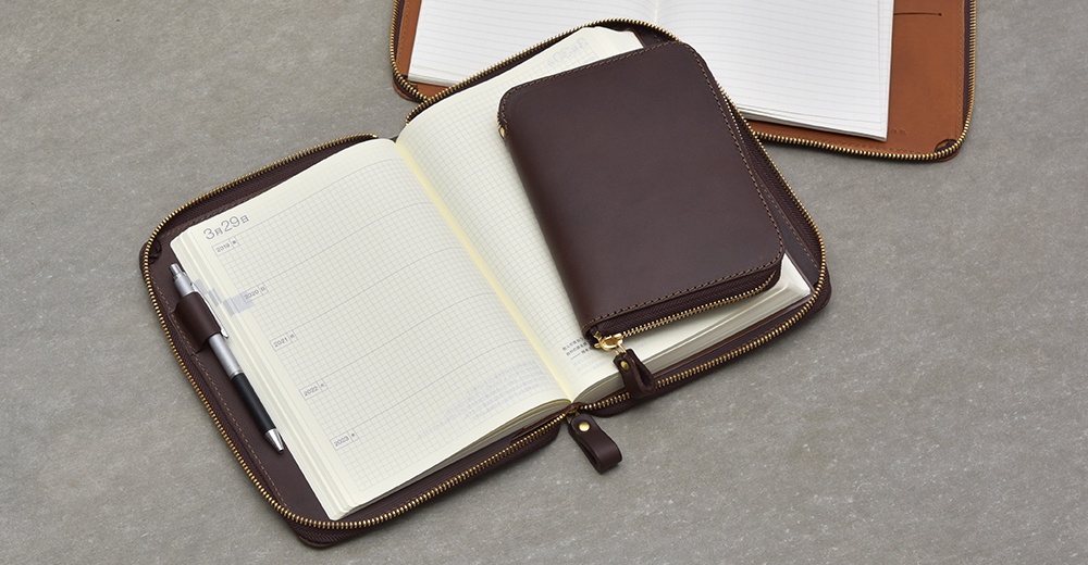 一個打開的深棕色皮革記事本收納包，裡面裝有筆記本和一支筆。