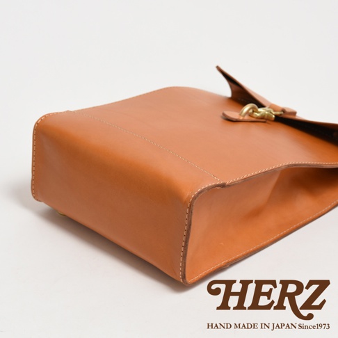 職人手作皮革紙袋風後背包，材質為天然皮革，呈現自然棕色，簡約的設計搭配金屬扣環，側面縫線清晰。