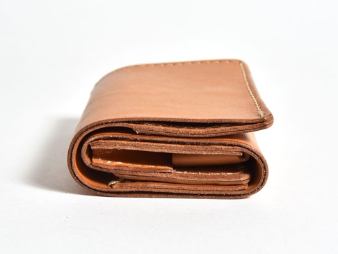 一個棕色皮革三折式迷你短夾，展示其層疊的結構和精緻的縫線。