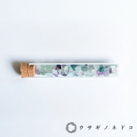 玻璃試管瓶裝有大量淺綠色、淡紫色和透明色的小塊礦石，瓶口由軟木塞封閉。