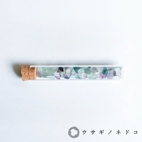 玻璃試管瓶裝有大量淺綠色、淡紫色和透明色的小塊礦石，瓶口由軟木塞封閉。