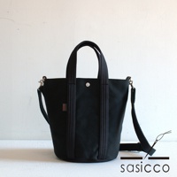 黑色三河木綿刺子織兩用水桶包，配有頂部提把和可拆卸肩帶，包身織紋清晰，正面有紅色品牌標籤。