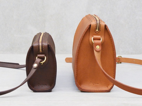 兩個皮革拉鍊單肩包，一個深棕色，一個棕褐色，皆為圓潤的造型，配有金色拉鍊和皮革背帶。