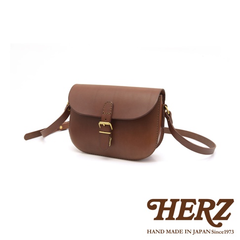 職人手作皮革經典馬鞍包，呈現深棕色皮革，設有黃銅扣環和可調式肩帶。