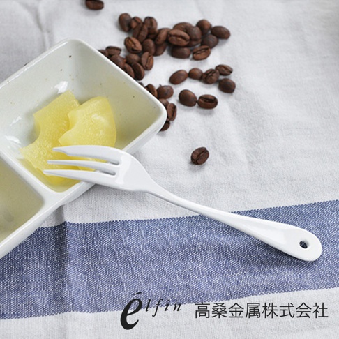 日製白琺瑯材質的單支水果叉，三叉設計，手柄末端有掛孔，搭配白色陶瓷分格盤中的水果塊和散落的咖啡豆。