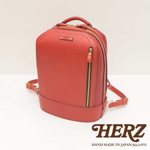 紅色皮革立體商務後背包，採用手工縫製，正面設有拉鍊口袋，搭配金色五金配件。